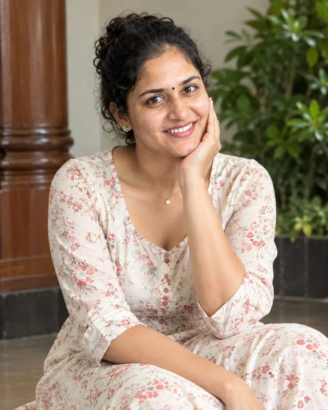 Aarti laughing in a pale floral kurta, chin resting on her hand