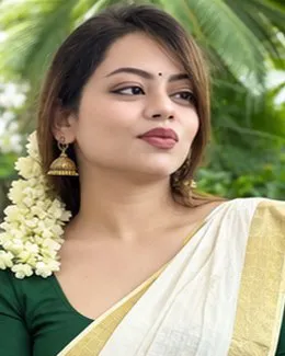 Riya in a cream saree with a green blouse, looking off to the side