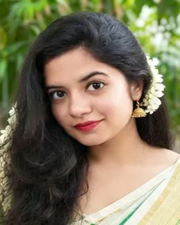 Lakshmi in a cream saree, outdoors under green trees